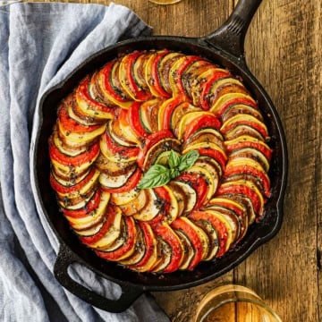 An overhead view of a serving of cast-iron skillet ratatouille with concentric layers of evenly slice eggplant, zucchini, squash, and tomatoes.