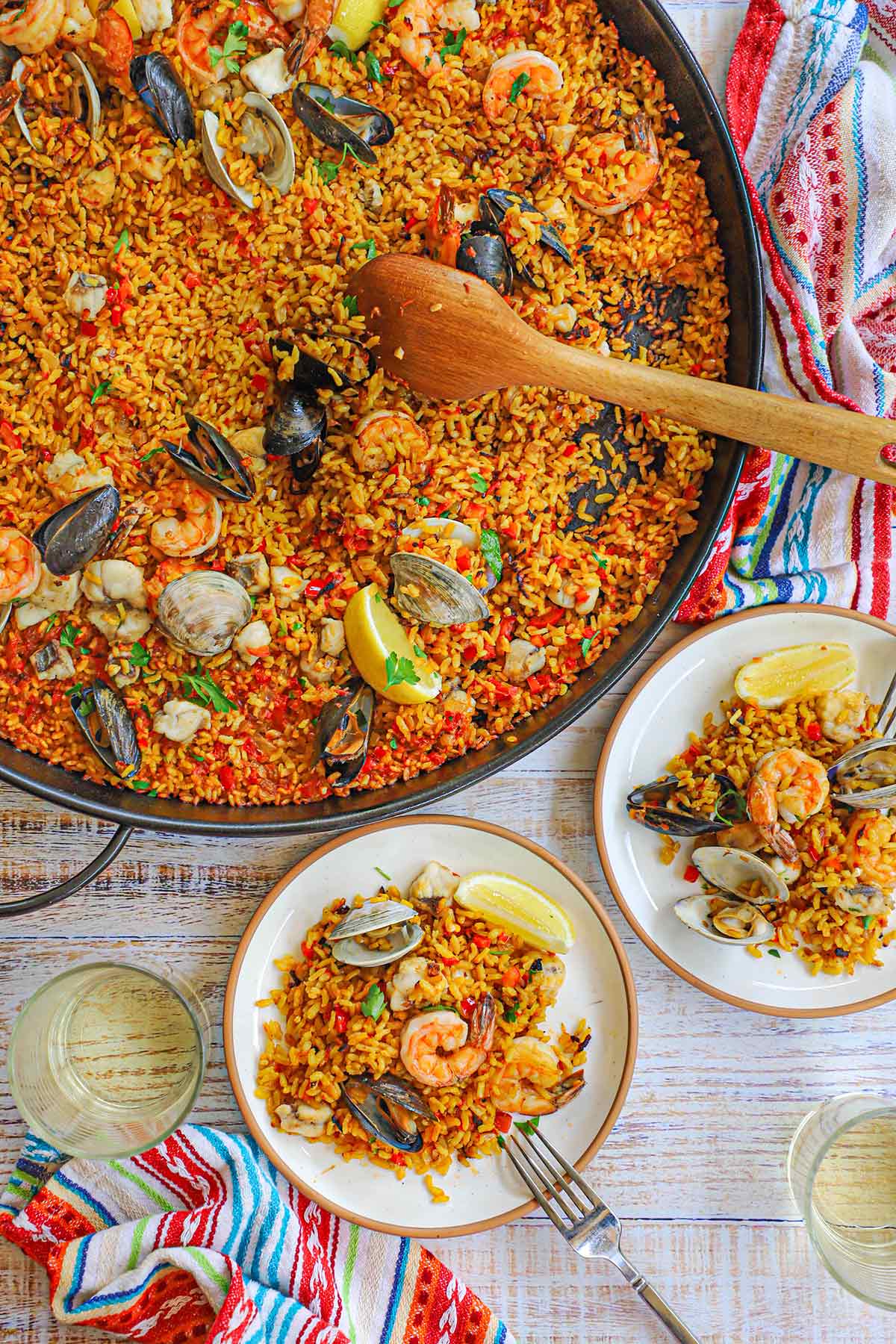 An overhead view of a large paella pan filled with seafood paella next to small tapas-style plates filled with small servings of the paella.