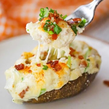 A person using a fork to lift the filling out of a twice baked potato that is resting on a white salad plate.