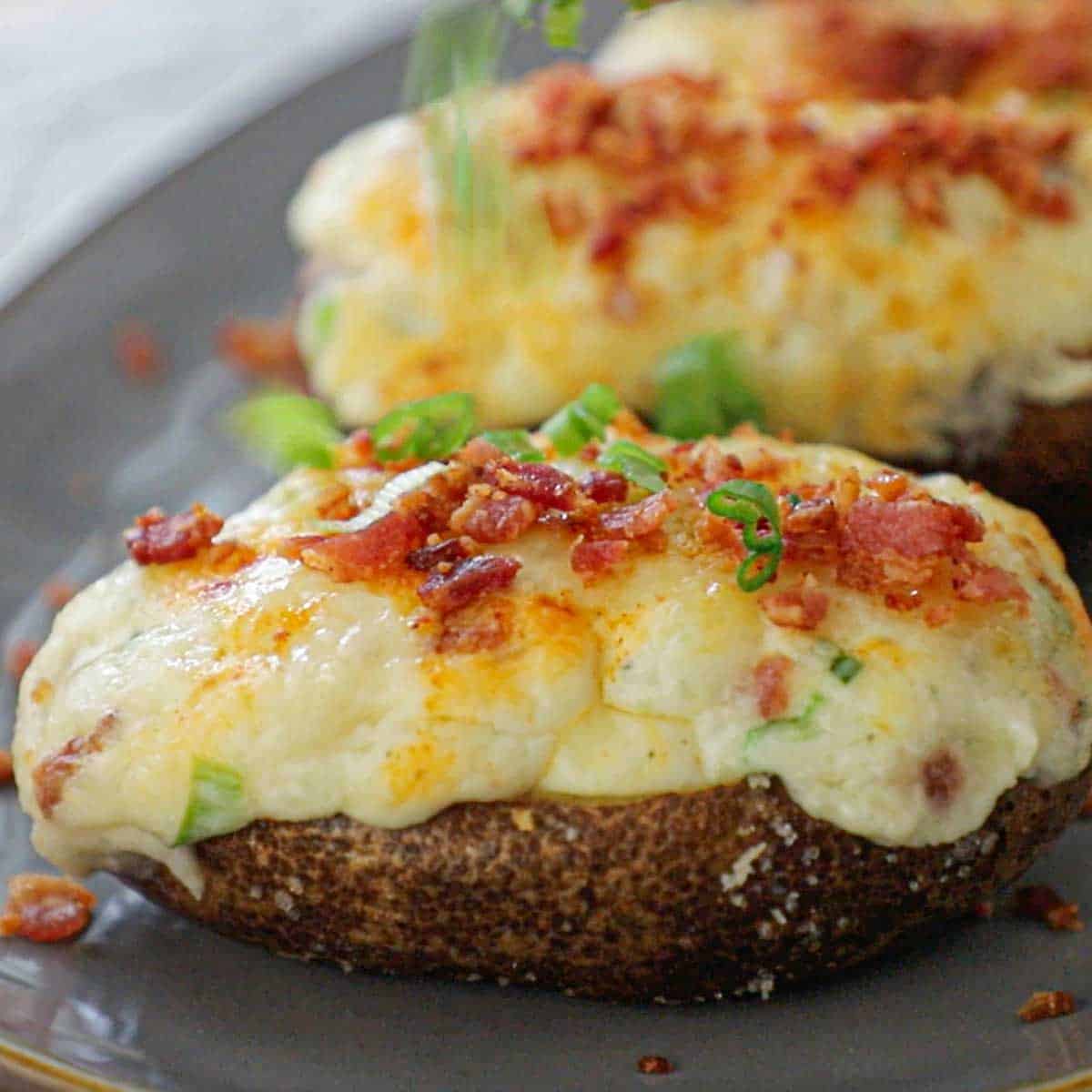 A person sprinkling chopped scallions over the tops of twice baked potatoes that are also topped with crispy bacon bits.