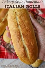 A person holding a bakery-style homemade Italian roll in the palm of his hand.