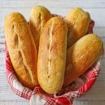 A color red and white linen-lined bread basked filled with a pile of homemade Italian rolls.