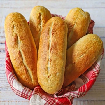 A color red and white linen-lined bread basked filled with a pile of homemade Italian rolls.