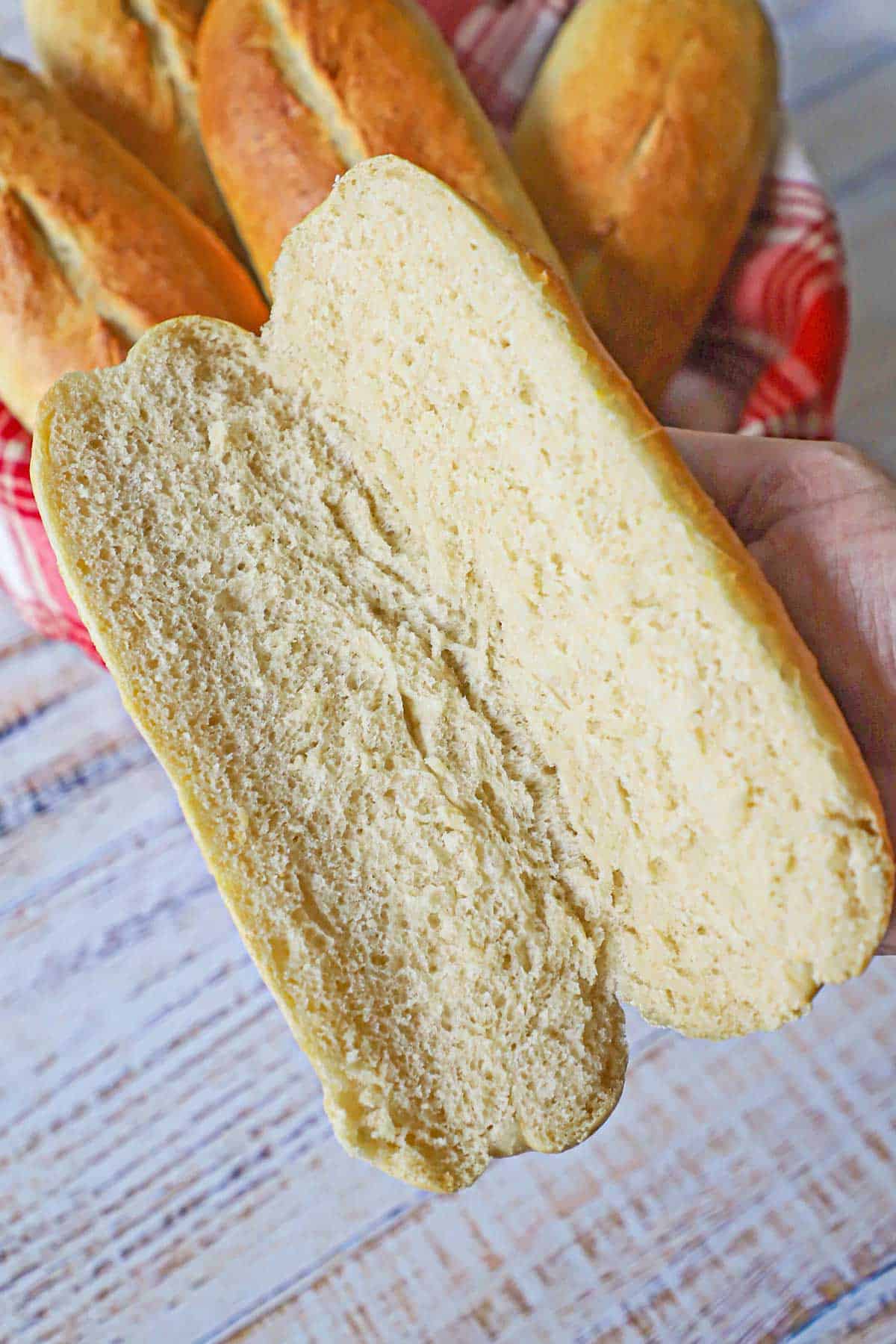 A person holding a homemade Italian roll that has been split open lengthwise revealing the soft crumb interior of the bread.