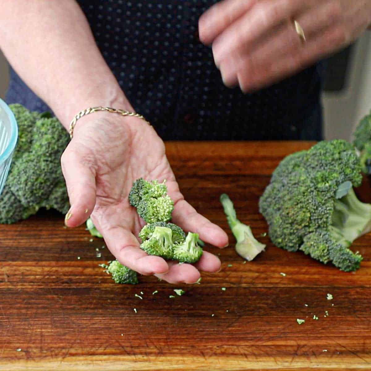A person holding small florets of broccoli that we just cut from a broccoli crown on a wooden cutting board.