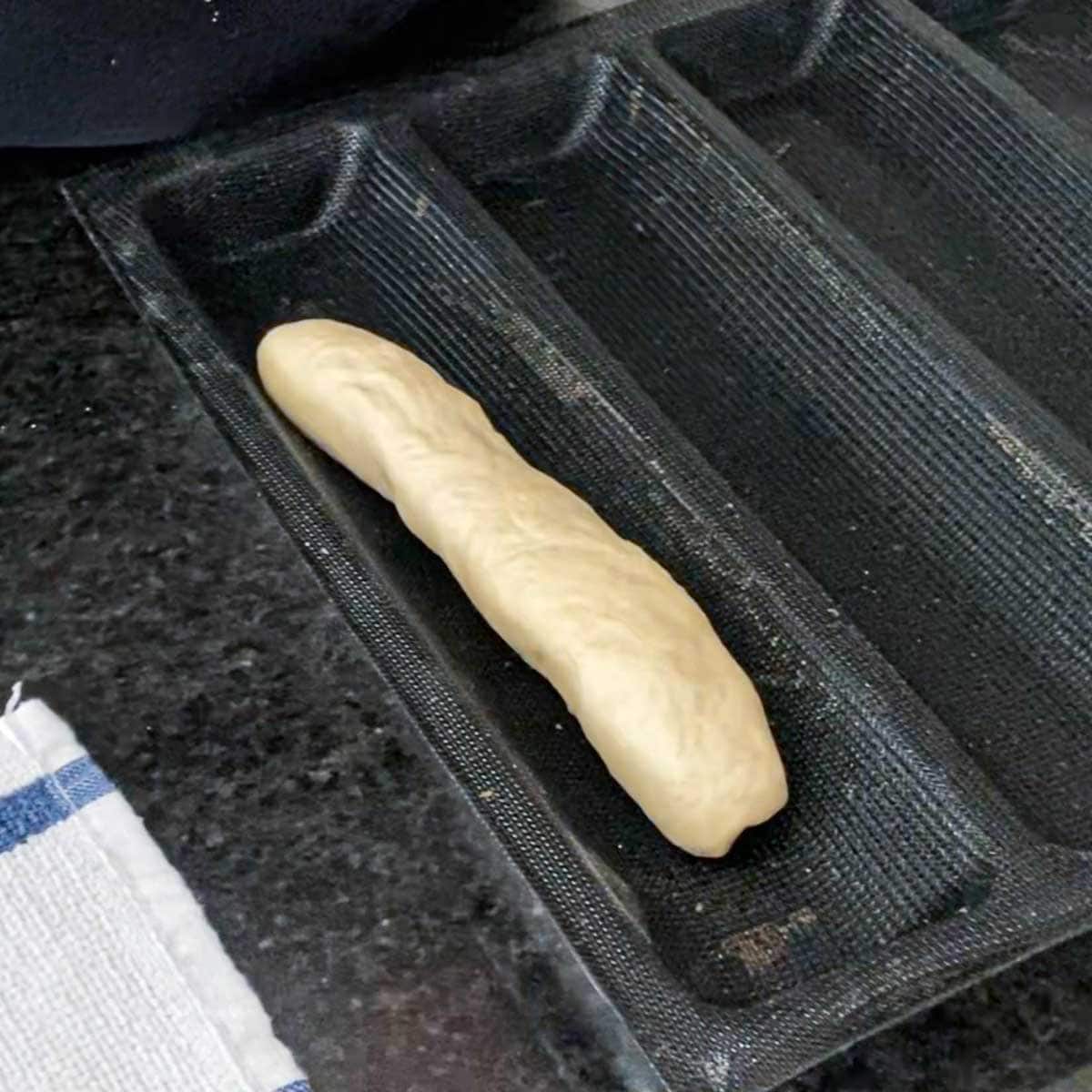 A 10-inch cylinder of Italian rolls dough that has been placed in the channel of a silicone baking mat.