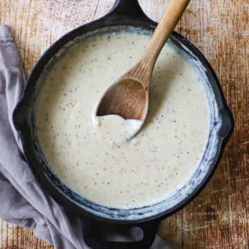 An overhead view of Classic Cream Gravy in a black cast-iron skillet with a wooden spoon resting in the middle of the pan.