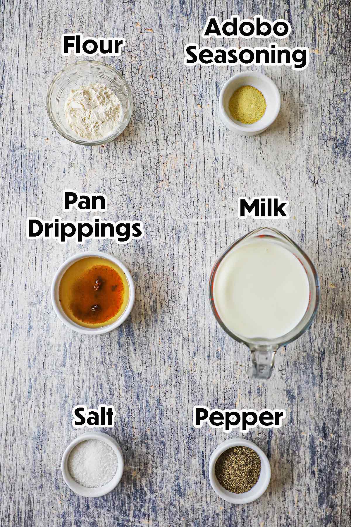 An arrangement of ingredients for Classic Southern Cream Gravy on a grey wooden background including milk, pan drippings, flour, and seasonings.