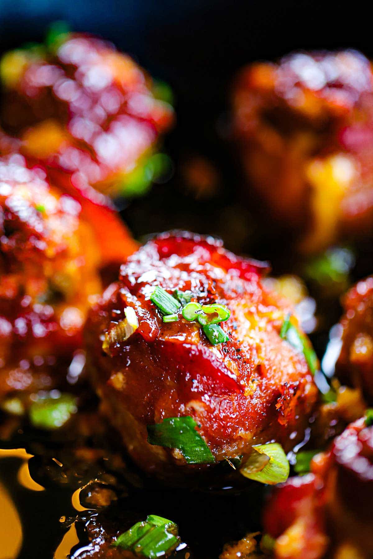 A close-up view of a smoked bacon-wrapped meatball with cheddar and jalapeño in a cast-iron skillet with chopped scallions sprinkled on top.