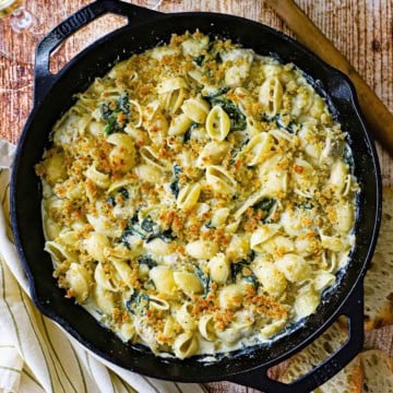 An overhead view of a large cast-iron skillet filled with freshly prepared Spinach Artichoke Dip Pasta topped with a toasty Panko breadcrumb mixture.