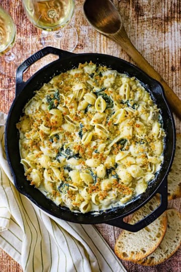 An overhead view of a large cast-iron skillet filled with freshly prepared Spinach Artichoke Dip Pasta topped with a toasty Panko breadcrumb mixture.