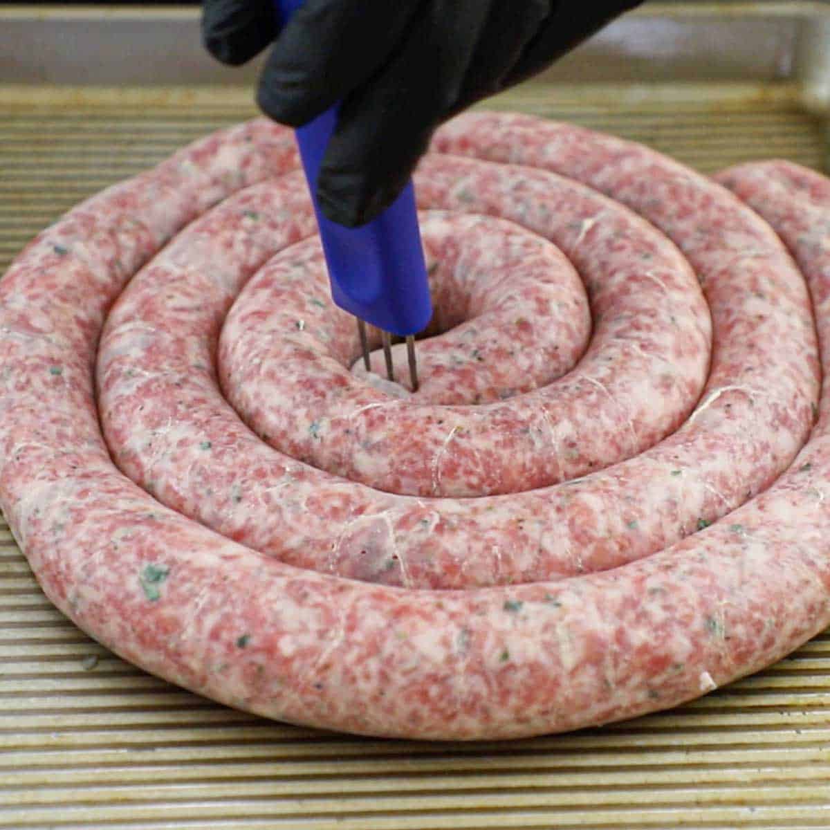 A person using a sausage pricker to pop visible air pockets out of freshly stuffed Italian sausage link on a metal sheet pan.