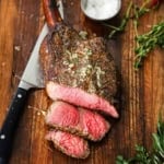 A close-up view of a tomahawk steak with roasted bone marrow butter that has two slices cut from it resting on a wooden cutting board.