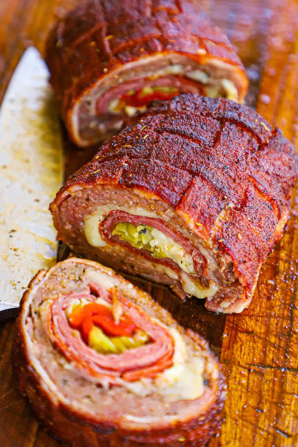 A Smoked Italian Fatty that has been cut into three large pieces revealing the braided topping, and the layers of Italian meat, cheese, and pickled veggies inside.
