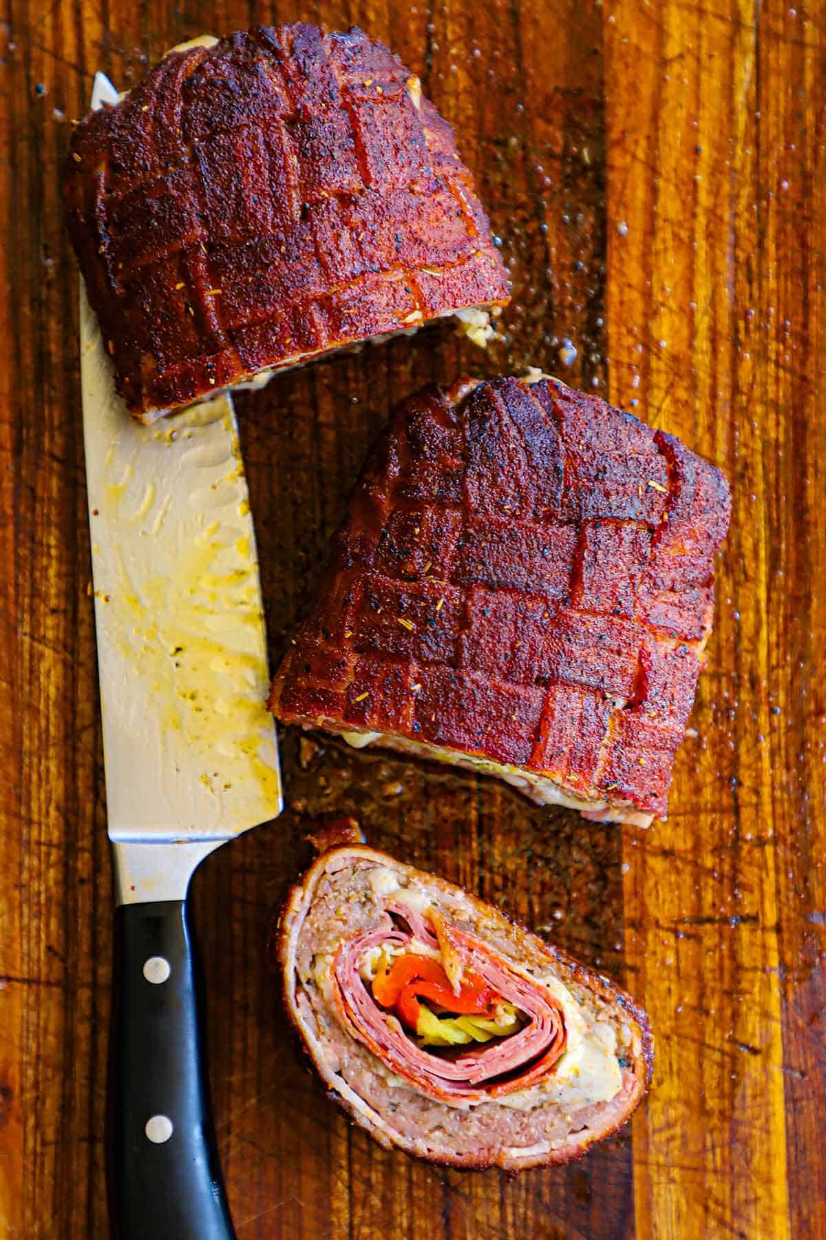 An overhead view of three large pieces of a Smoked Italian Fatty that with one piece laying on its side revealing the layers of Italian meat, cheese, and roasted veggies on the inside.