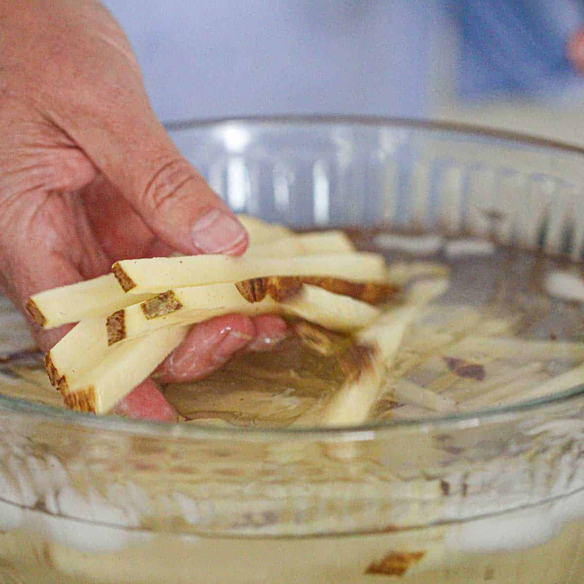A person swishing strips of russet potatoes in a bowl filled with water.