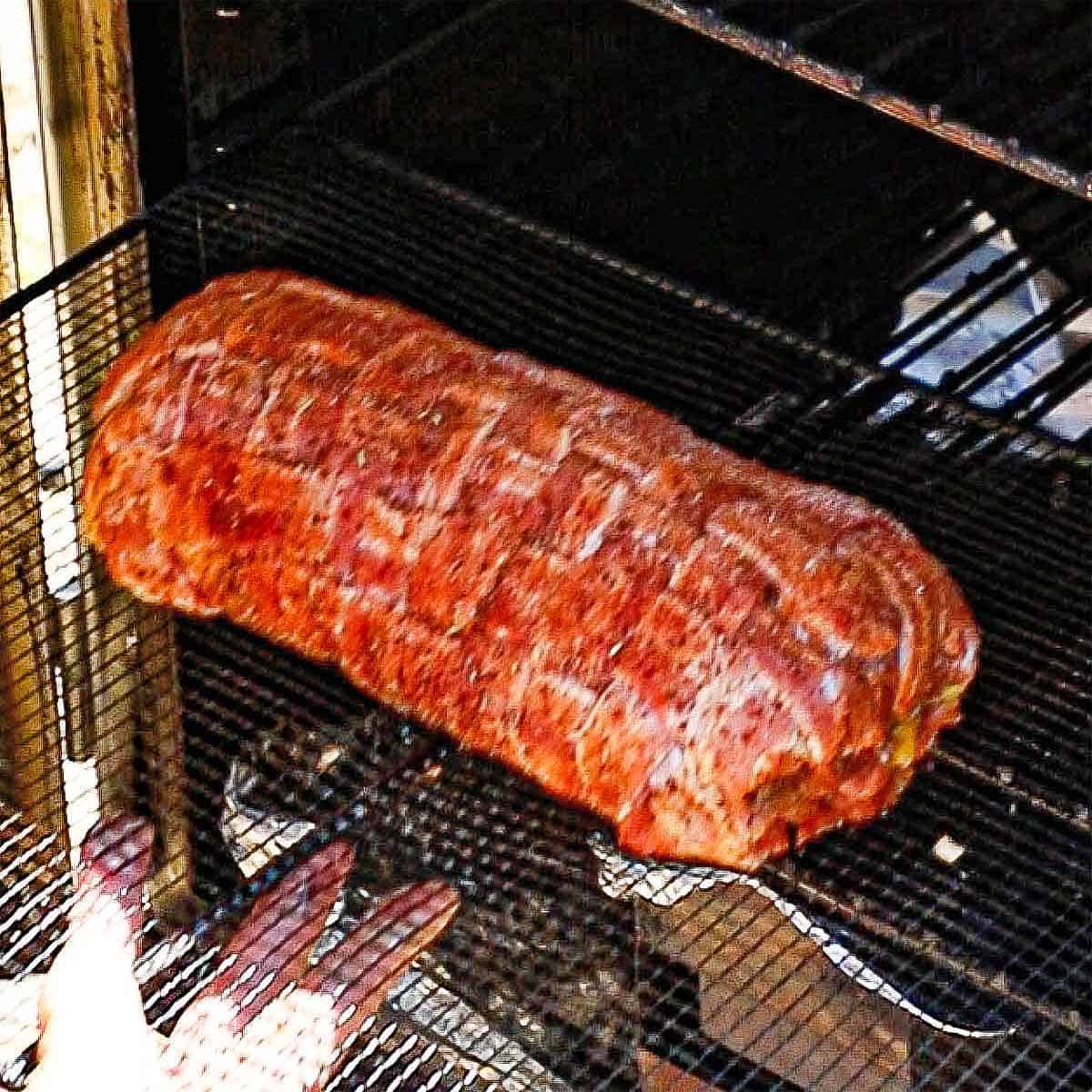 A person pulling a smoked Italian fatty from an electric smoker after it has been fully cooked.
