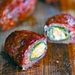 A straight-on view of smoked armadillo eggs on a cutting board with one of them split open to reveal the melty cheese, jalapeño peppers, and sausage encasing it all.