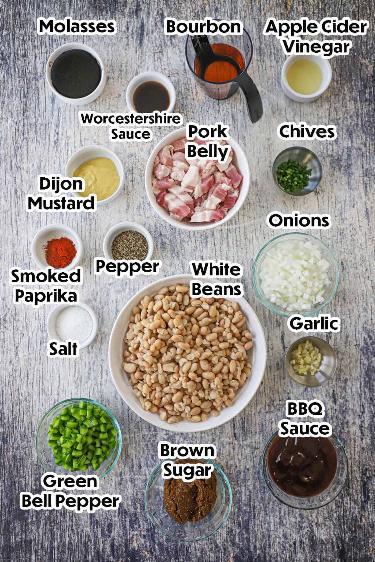 An arrangement of ingredients for bourbon-glazed baked beans with pork belly including white beans, pork belly, onions, bell peppers, brown sugar, BBQ sauce, garlic, Bourbon, molasses, Worcestershire sauce, vinegar, and seasonings.