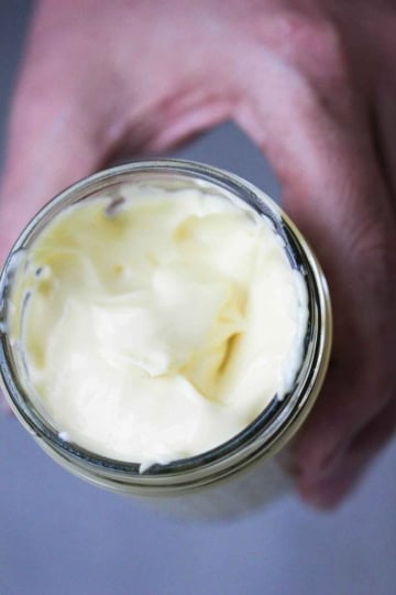 A person holding a glass jar that is filled to the top with homemade mayonnaise.