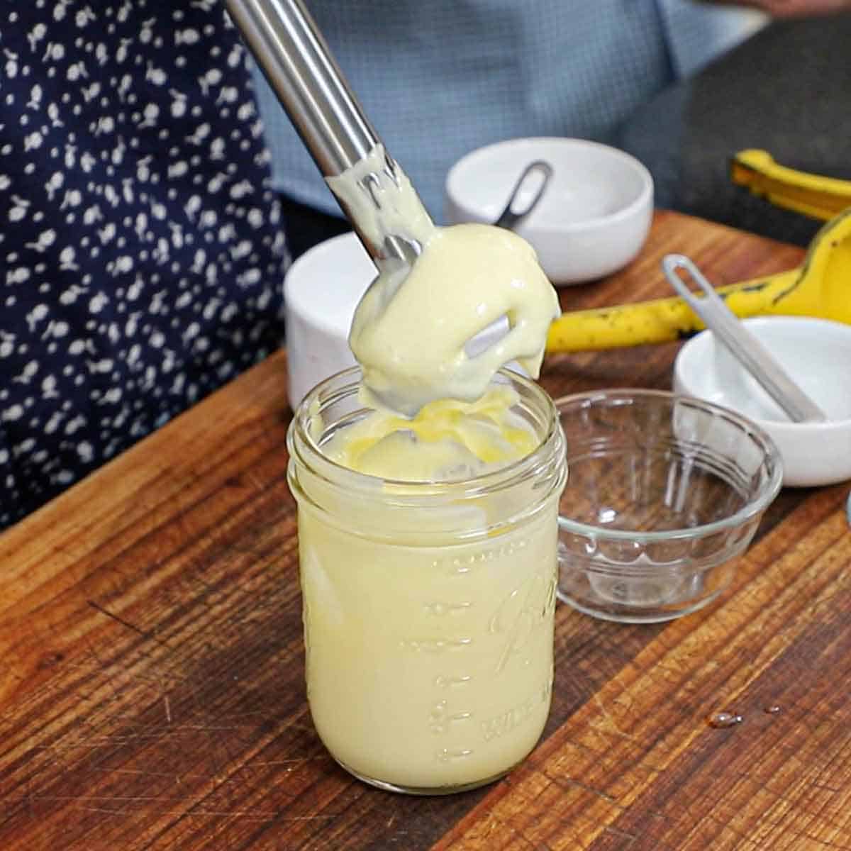 A person pulling an immersion blender out of a jar of freshly made homemade mayonnaise.