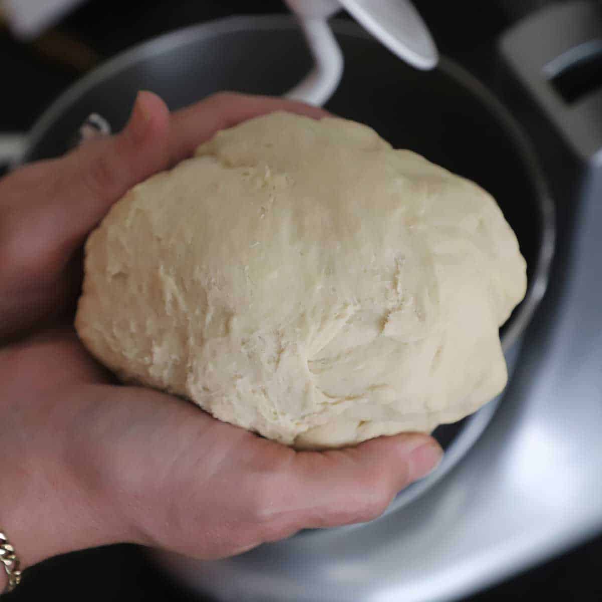 A person using his hands to form pizza dough into a smooth ball over a stand-mixer.