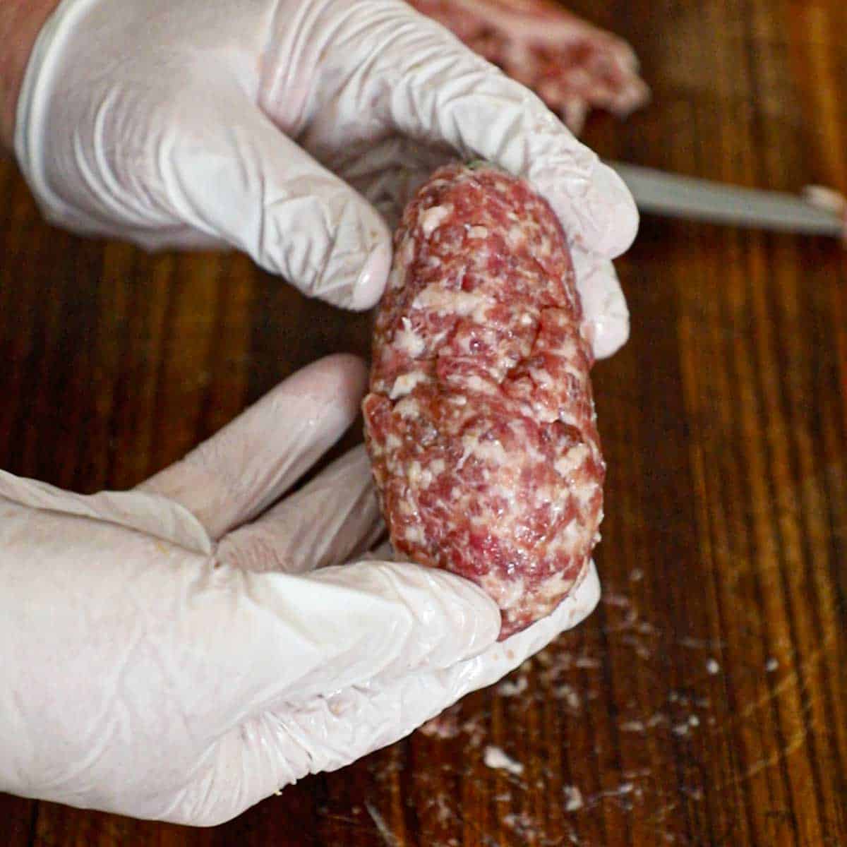 A person holding a smoked armadillo egg that has been encased in raw Italian sausage and is about to go into the smoker.