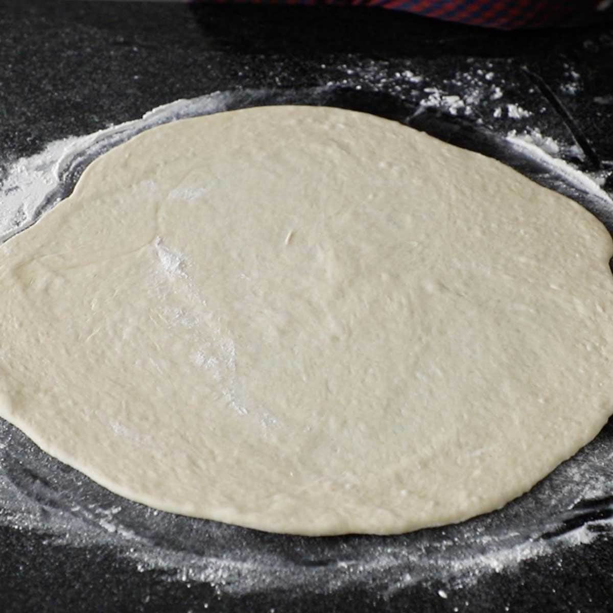Pepperoni roll dough that has been rolled out into a 14-inch circle on a lightly flour black marble surface.