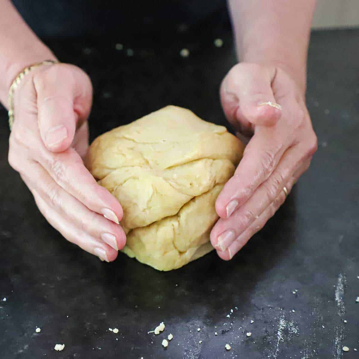 A person using two hands to form an empanada dough into a bowl on a black marble surface.