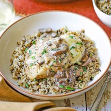 A close-up view of a bowl filled chicken Gloria with a mushroom sauce poured over the top and resting on a bed of cooked wild rice.