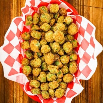 An overhead view of a basket lined with red and white-checkered paper and filled with Classic Southern Fried Okra.