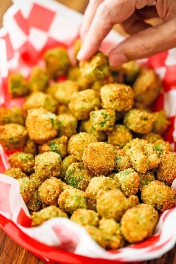 A person using his fingers to pick up a piece of Classic Southern Fried Okra from a basket filled with the same.