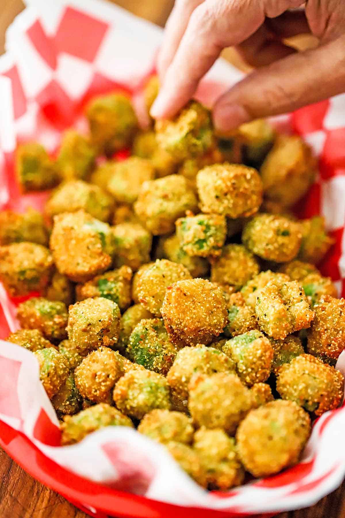 A person using his fingers to pick up a piece of Classic Southern Fried Okra from a basket filled with the same.