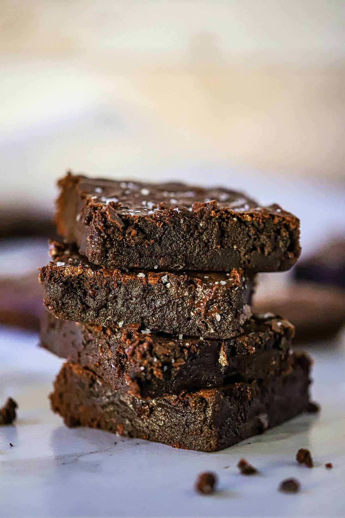 A stack of four ultimate fudge brownies with coarse sea salt sprinkled on the top of each brownie.