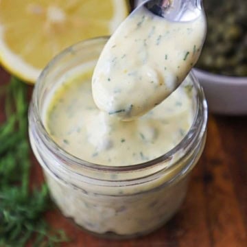 A close-up view of a spoon holding up a serving of Lemon-Dill and Caper Aioli over a small jar containing the same.