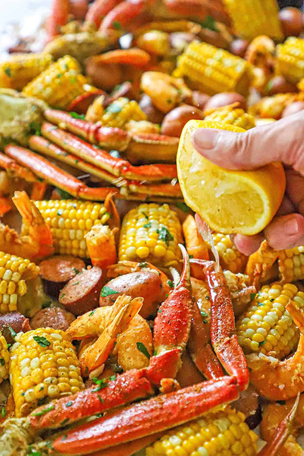 A person squeezing half of a lemon over the top of a large serving of Louisiana Seafood Boil stretched across white butcher paper.