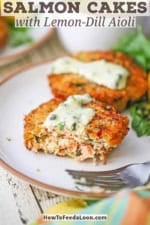 A close-up view of a half-eaten Salmon Cake topped with a smear of Lemon-Dill Aioli on a white plate with another salmon cake in the background.