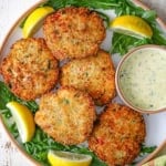 A close-up view of five freshly prepared fresh salmon cakes next to a small bowl holding Lemon-Dill and Caper Aioli.