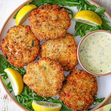 A close-up view of five freshly prepared fresh salmon cakes next to a small bowl holding Lemon-Dill and Caper Aioli.