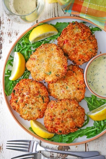 A close-up view of five freshly prepared fresh salmon cakes next to a small bowl holding Lemon-Dill and Caper Aioli.