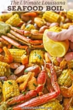 A person squeezing half of a lemon over the top of a large serving of Louisiana Seafood Boil stretched across white butcher paper.