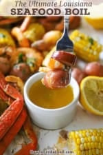 A person holding a fork that has a boiled red potato, shrimp, and slice of sausage on it over a small bowl of drawn butter.