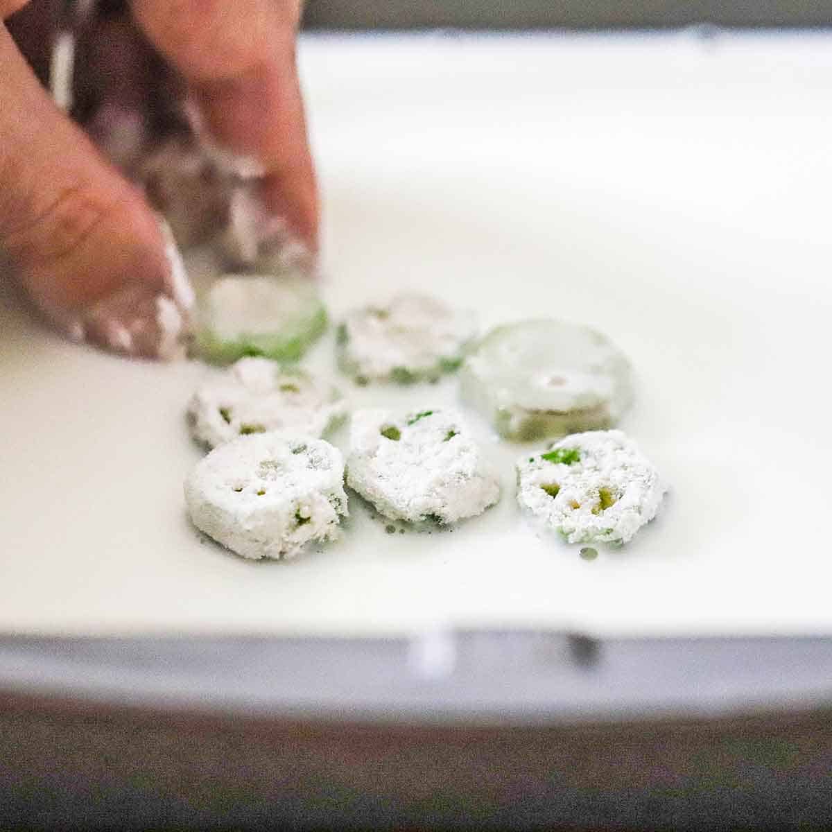 A person using his fingers to submerge sliced of okra that have been coated with flour in a pan filled with whole milk.