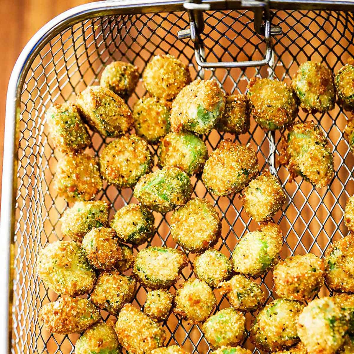 A person holding a fry basket over a cutting board that is filled with freshly fried Southern Fried Okra.