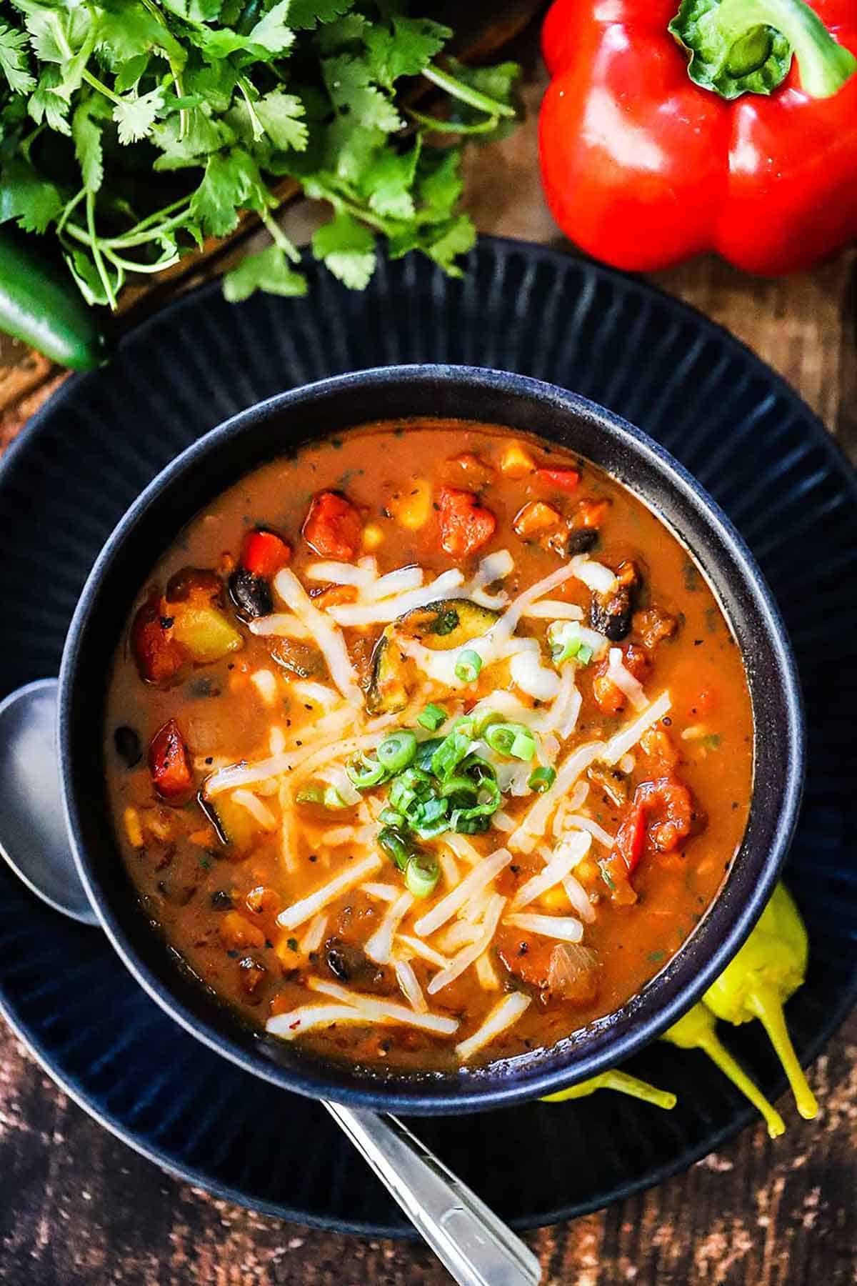 An overhead view a blue soup bowl filled with a serving of Vegetable Chili and Black Beans garnished with shredded Monterey Jack cheese and chopped cilantro.