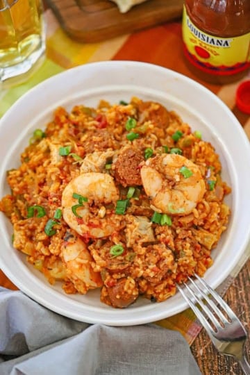 An straight-on view of a white bowl filled with a serving of authentic jambalaya topped with seared shrimp, andouille sausage, and chopped scallions.