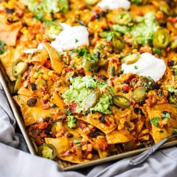 A close-up view of Sheet Pan Nachos topped with melty cheese, vegetarian chili, sliced pickled jalapeños, and dollops of sour cream and homemade guacamole