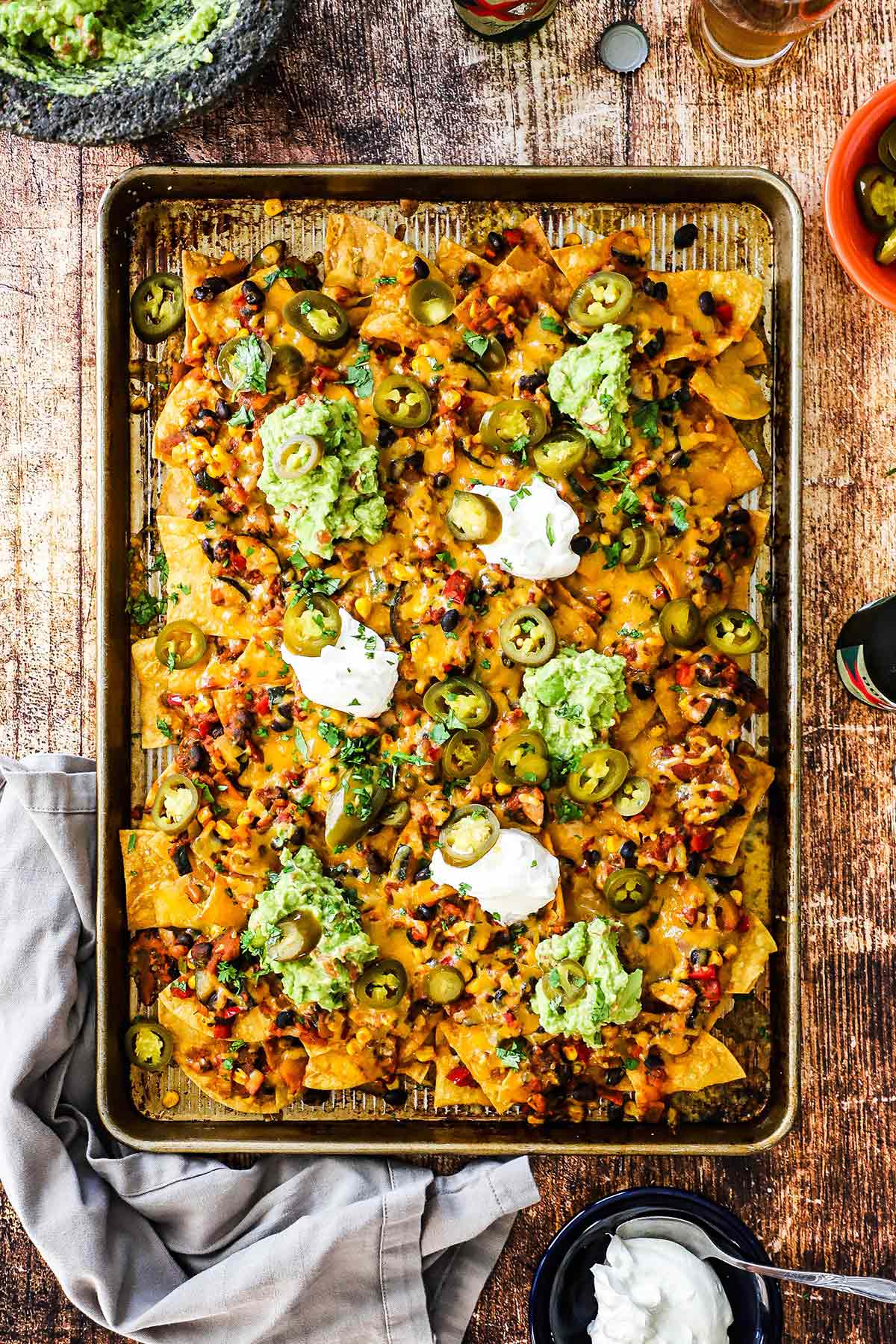 An overhead view of a large serving of Sheet Pan Nachos topped with vegetarian chili, melty cheese, and dollops of sour cream and homemade guacamole.