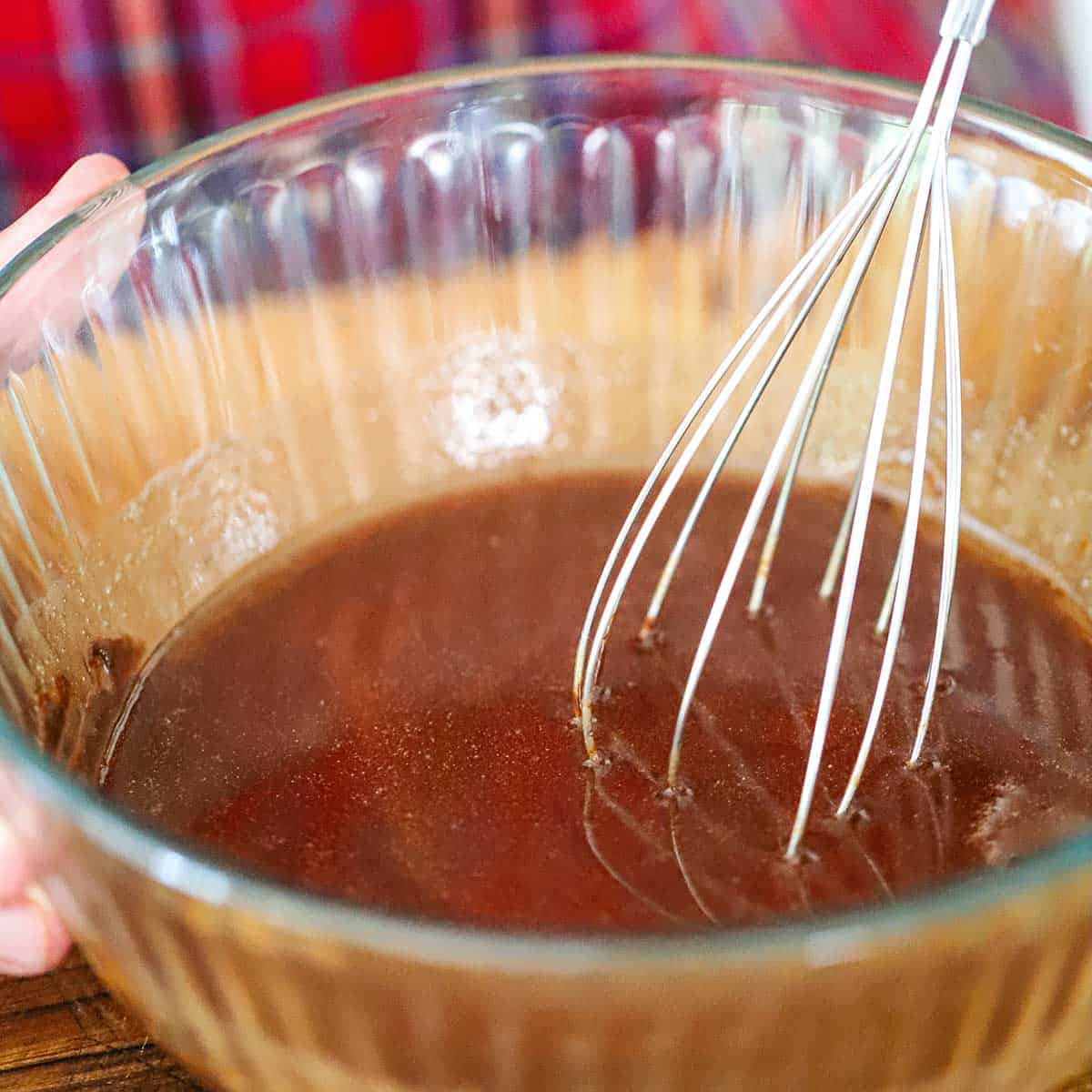 A person using a whisk to stir melted butter and semi-sweet chocolate in a glass bowl.