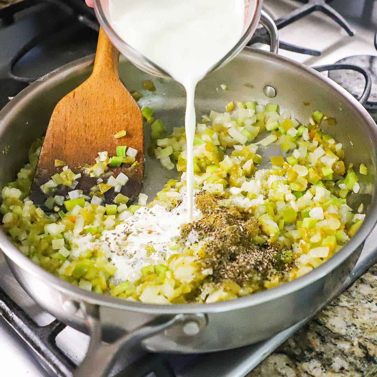 A person pouring heavy cream into a large skillet that is filled with sautéed peppers, onions, and seasonings.